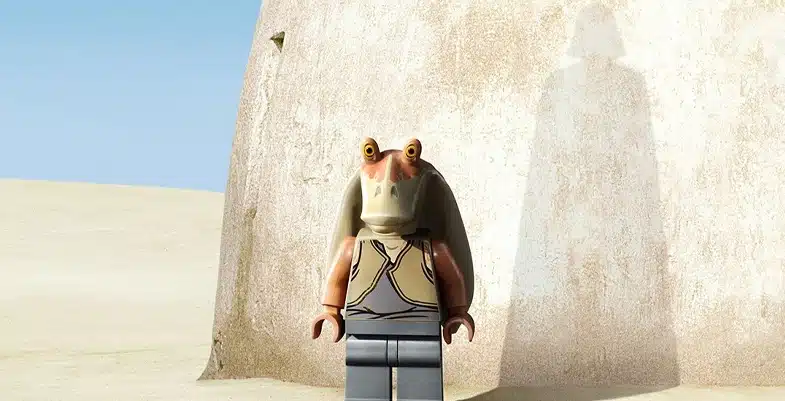 Figurine LEGO de Jar Jar Binks se tenant devant un mur dans un désert, avec une ombre évoquant Dark Vador projetée sur le mur.