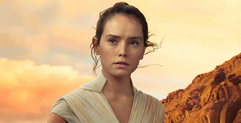 Rey Skywalker, est ici représentée en robe beige, observant l'horizon dans un environnement désertique avec un ciel orange au coucher du soleil.