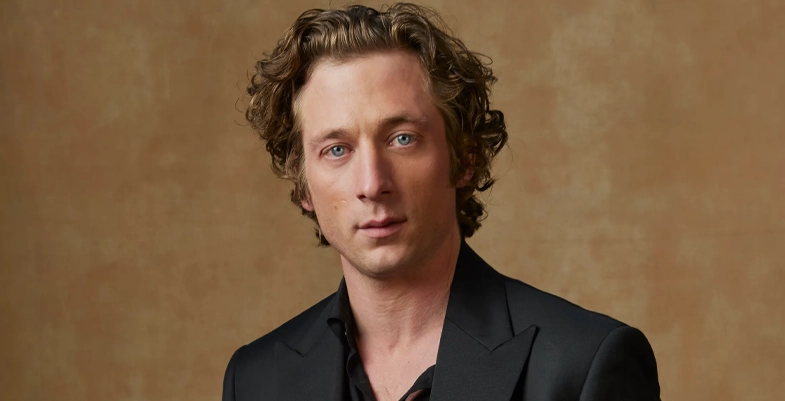 Jeremy Allen portant une veste noire, pose devant un fond neutre.